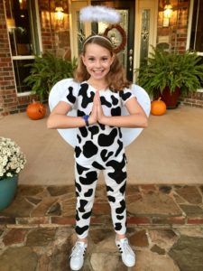 Girl dressed in cow print clothes with wings and a halo "holy cow"
