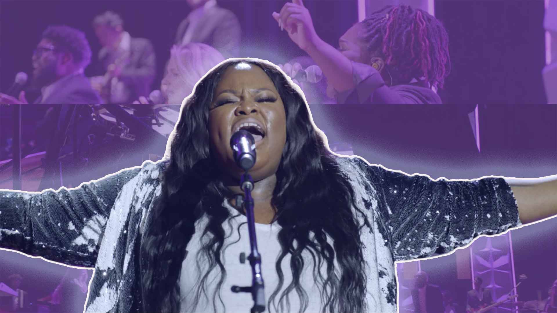 Tasha Cobbs Leonard in a Sequin Jacket Sings into a Microphone on a background with her worship band in concert